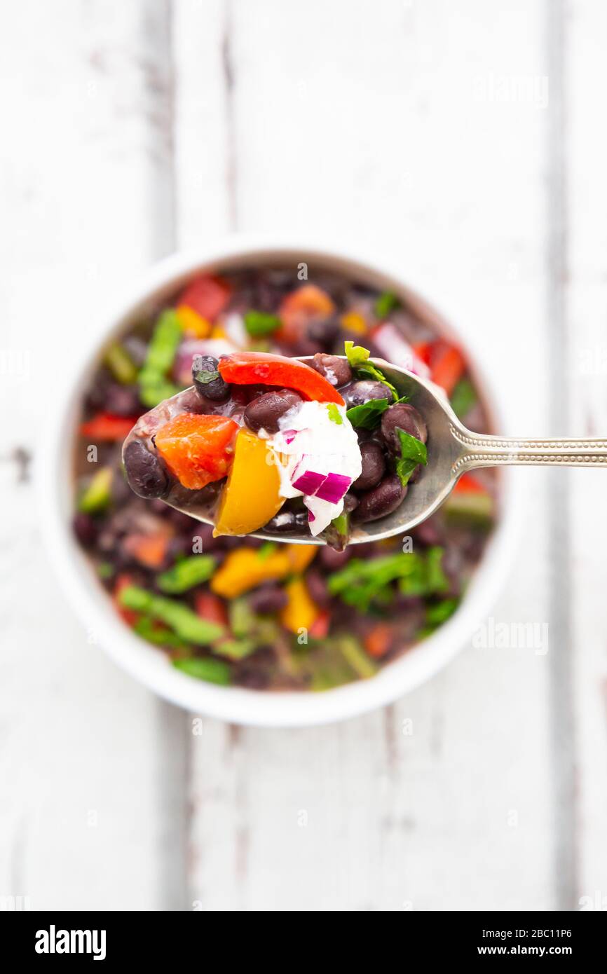 Spoon of black bean soup with bell pepper, cilantro, sour cream and red onions Stock Photo