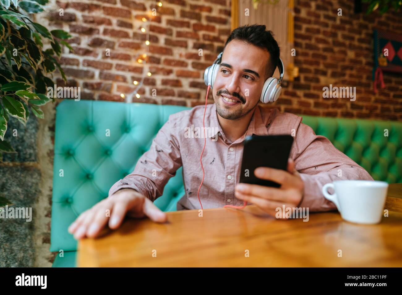 Smiling man in a cafe listening to music with headphones Stock Photo
