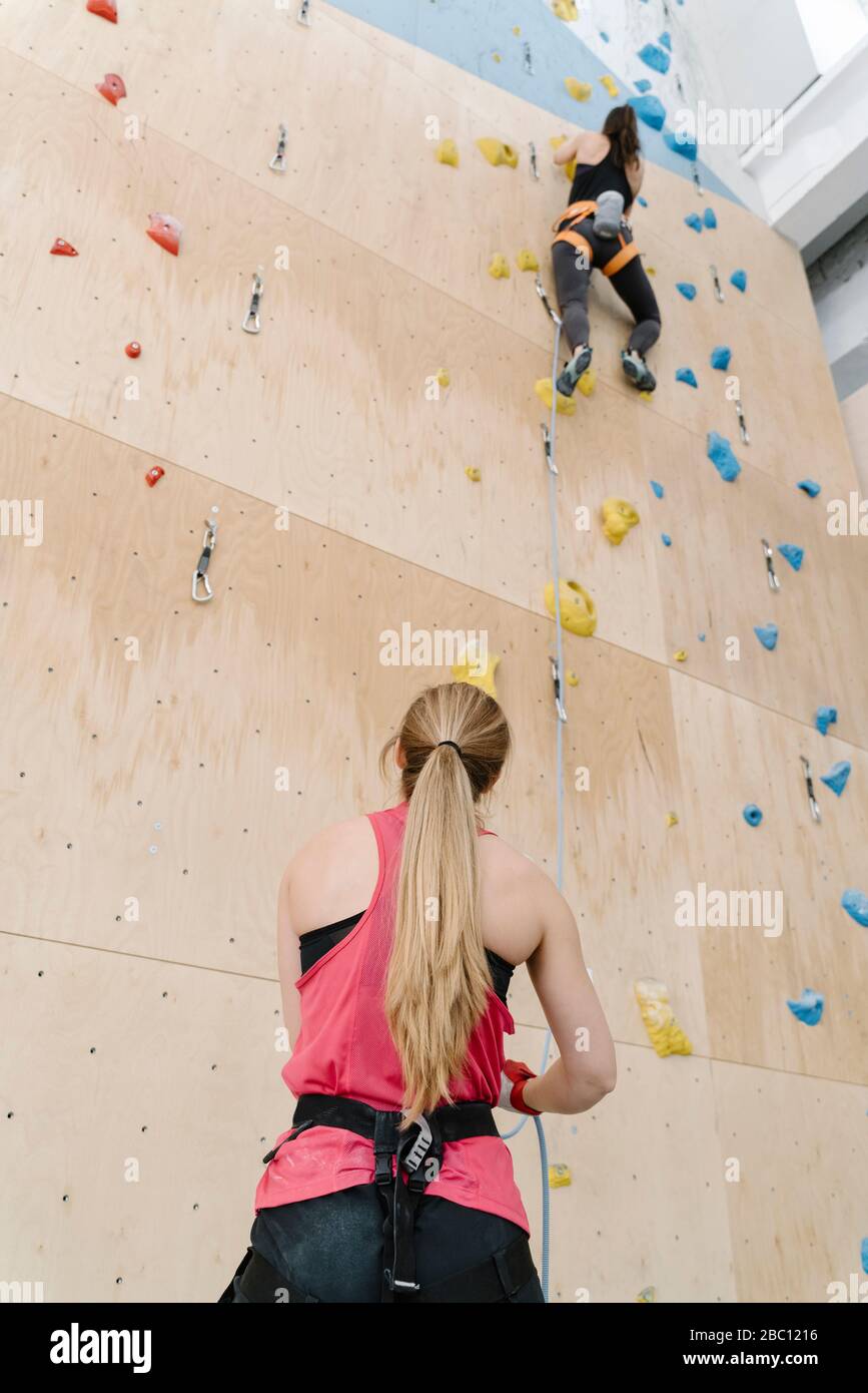 Woman with a rope securing partner on the wall in climbing gym Stock Photo