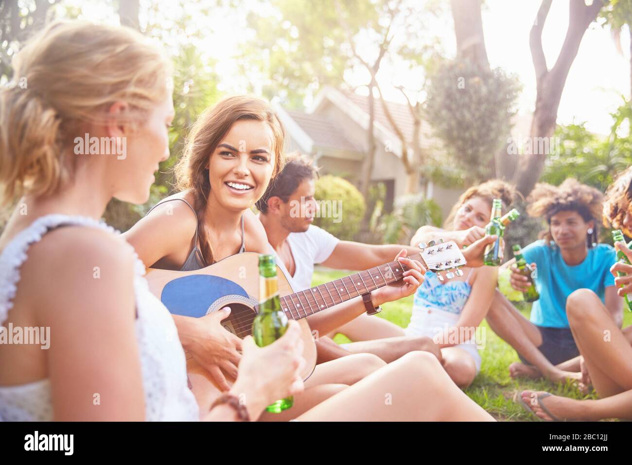 Young women friends hanging out, playing guitar and drinking beer in summer grass Stock Photo