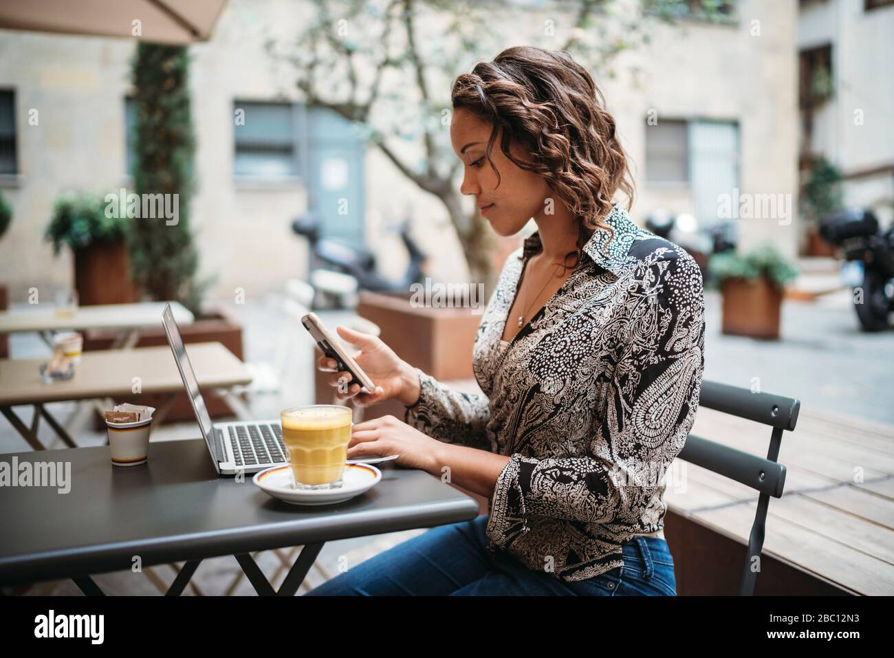 Young woman using laptop and smartphone at a pavement cafe Stock Photo ...