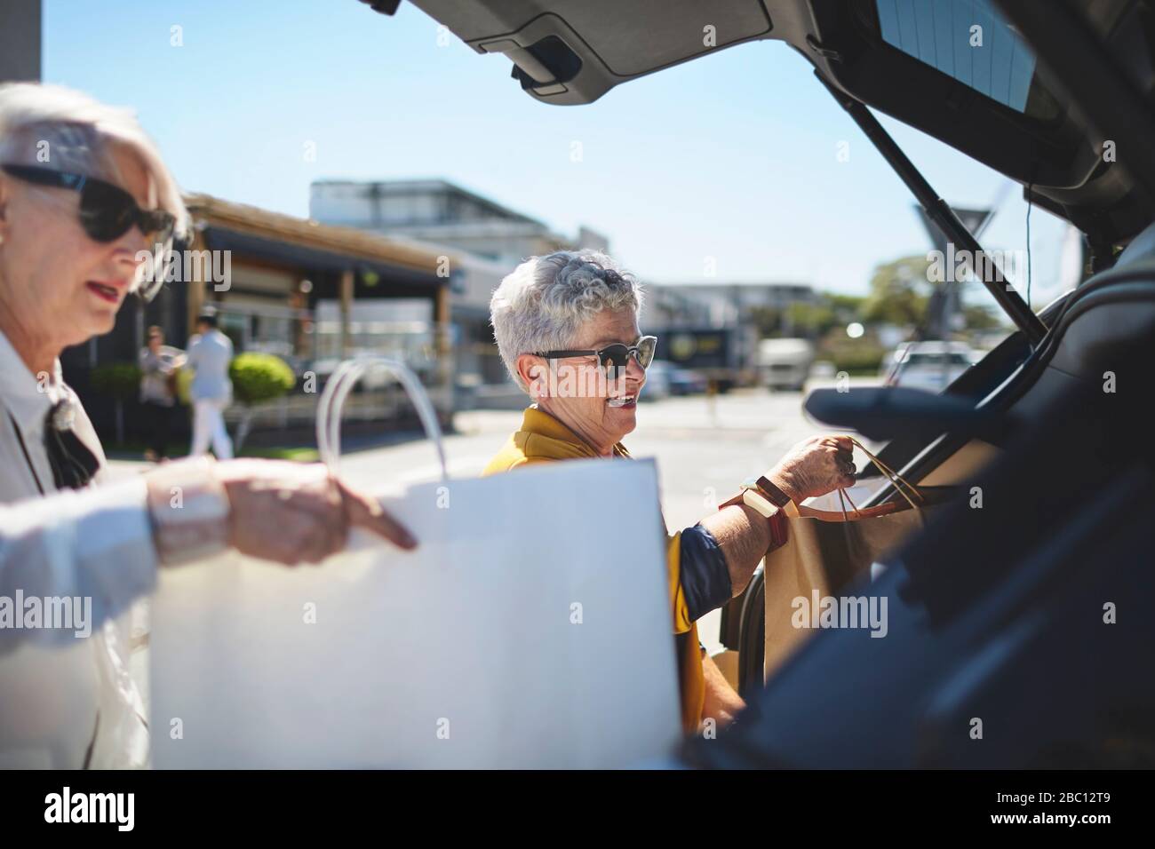 Senior women loading shopping bags into back of car in sunny parking lot Stock Photo