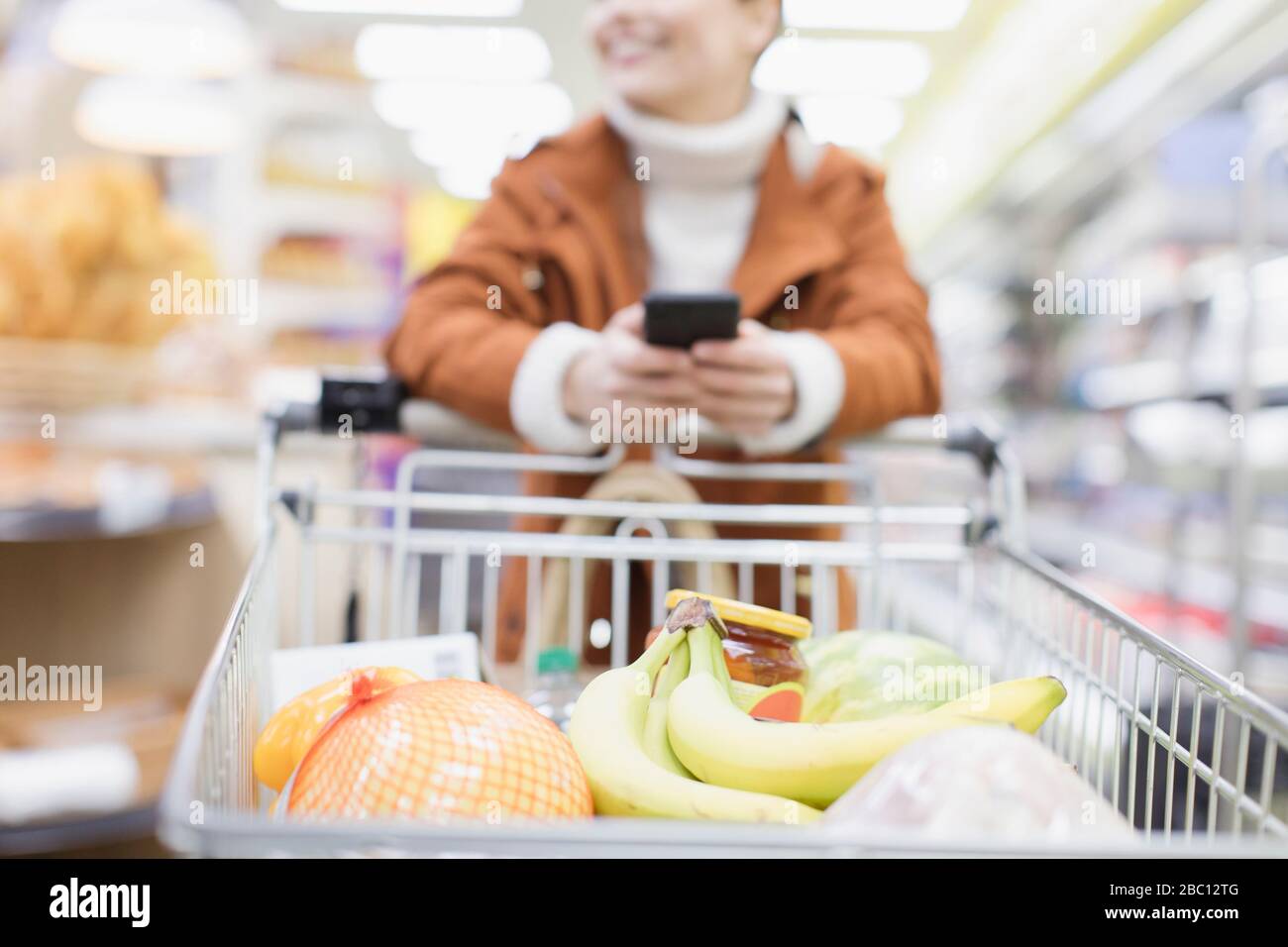 Woman with smart phone pushing shopping cart in supermarket Stock Photo ...