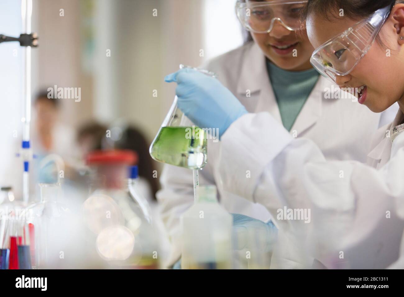 Girl students conducting scientific experiment, examining liquid in beaker in laboratory classroom Stock Photo