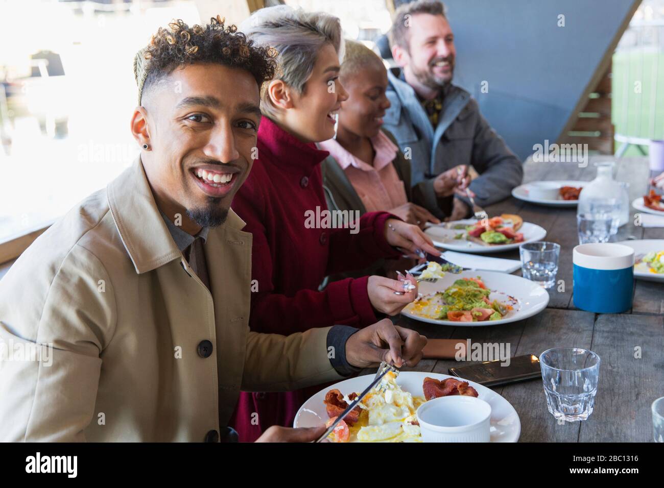 Portrait smiling young man eating breakfast with friends at restaurant outdoor patio Stock Photo