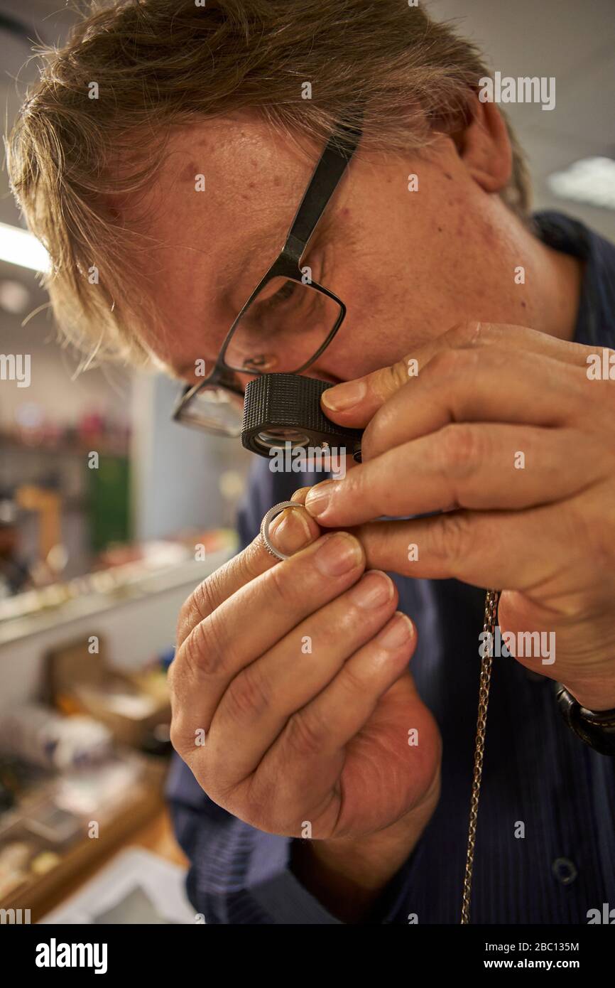Senior man checking the diamond on a ring with a magnifying glass Stock