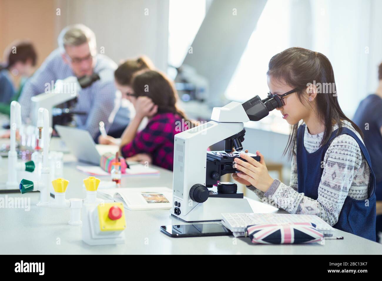 Girl student using microscope, conducting scientific experiment in laboratory classroom Stock Photo