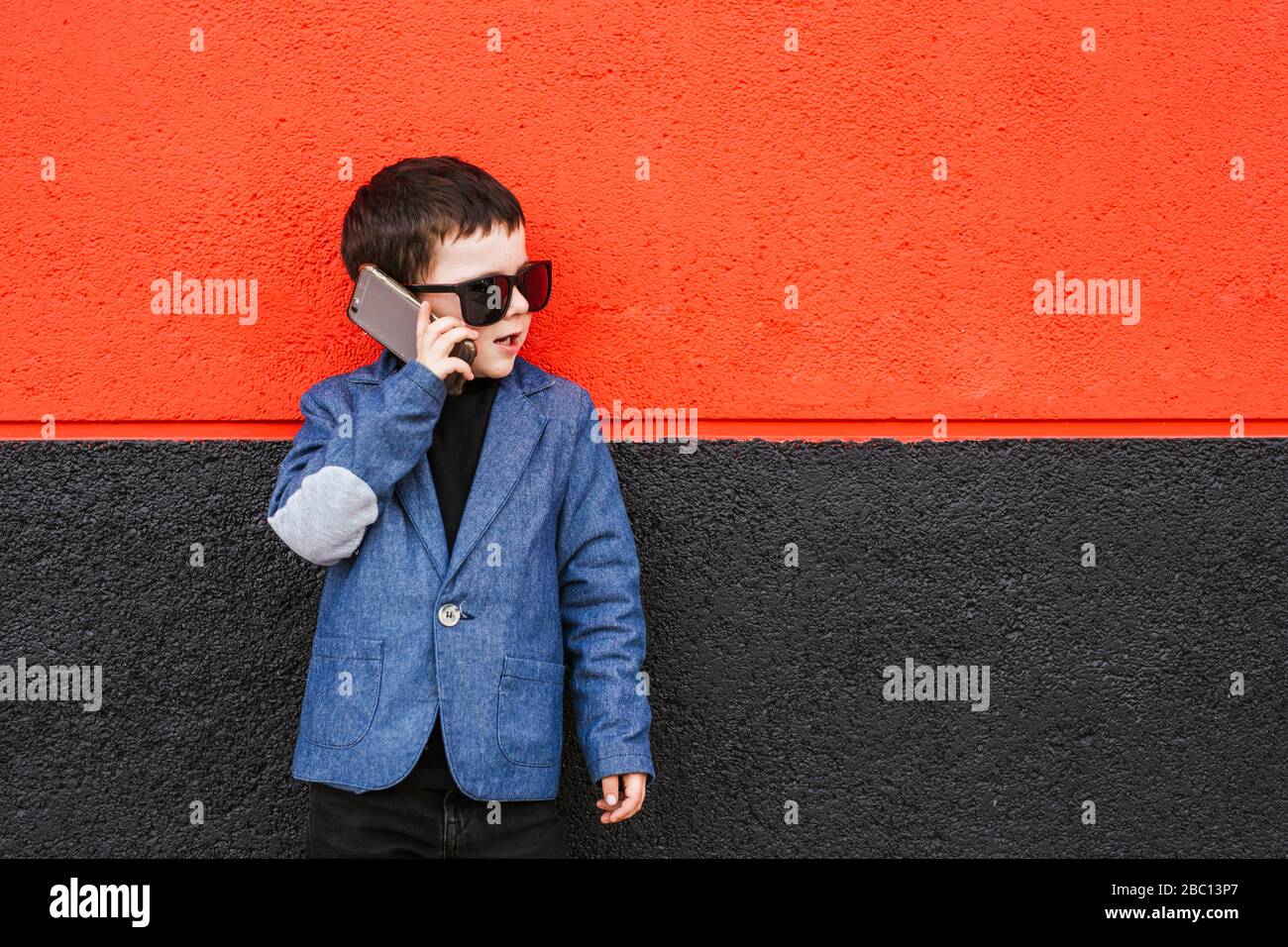 Portrait of little boy on the phone wearing suit coat and oversized sunglasses Stock Photo