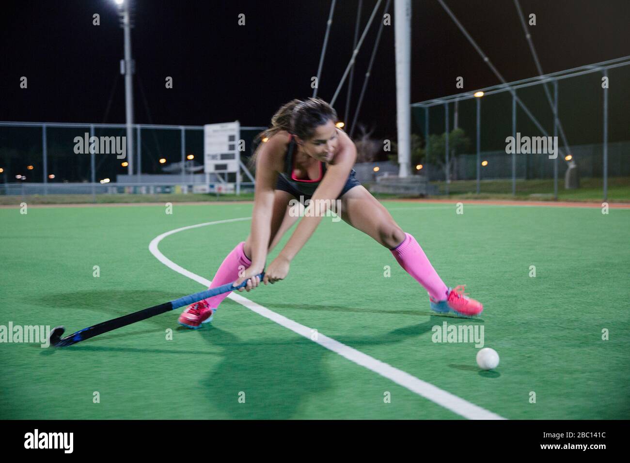 Determined young female field hockey player hitting the ball on field