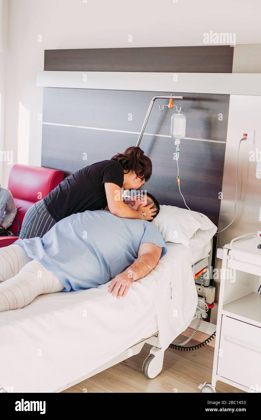 Daughter encouraging father lying in hospital bed Stock Photo