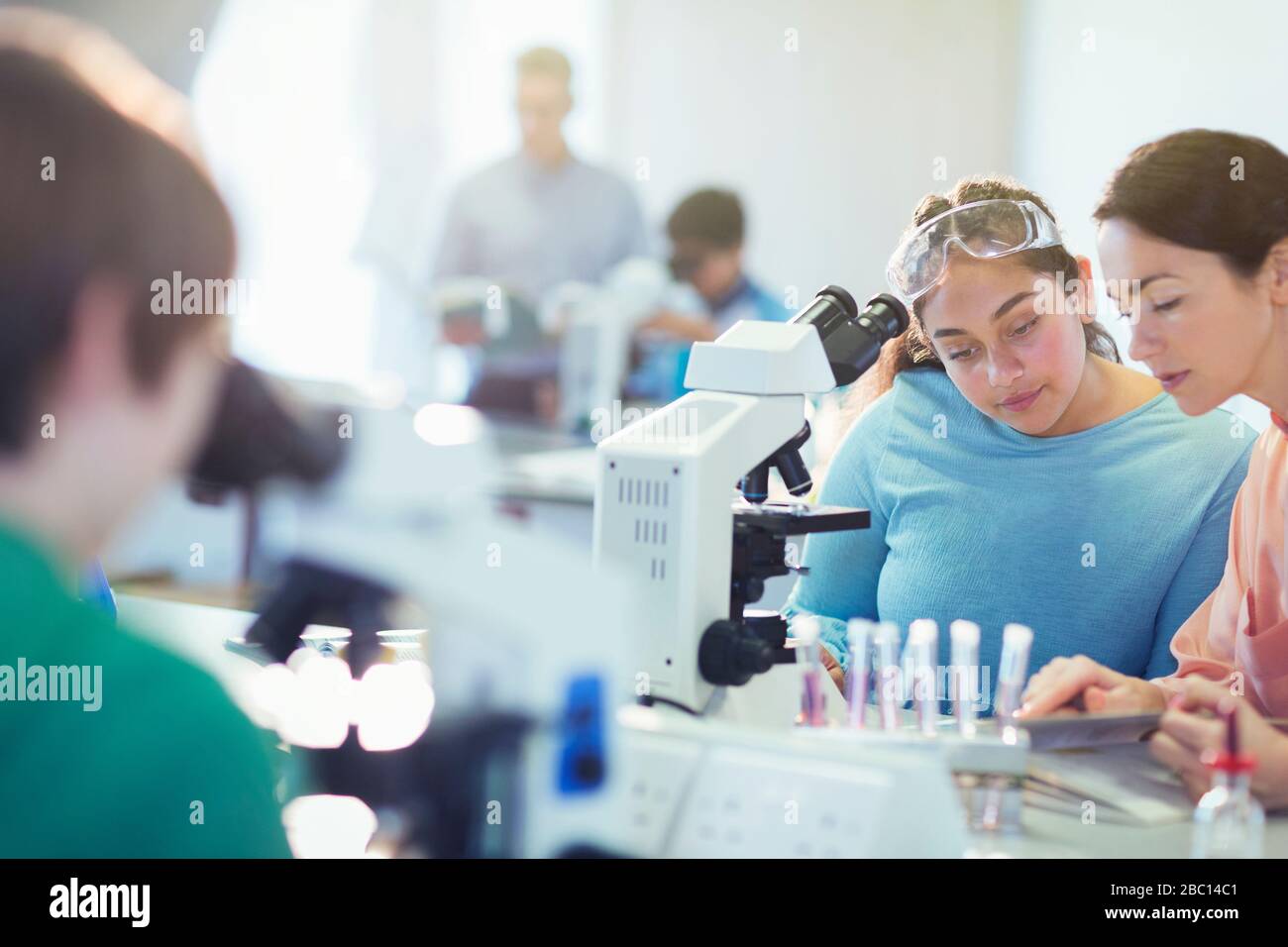 Female teacher and girl student conducting scientific experiment at microscope in laboratory classroom Stock Photo
