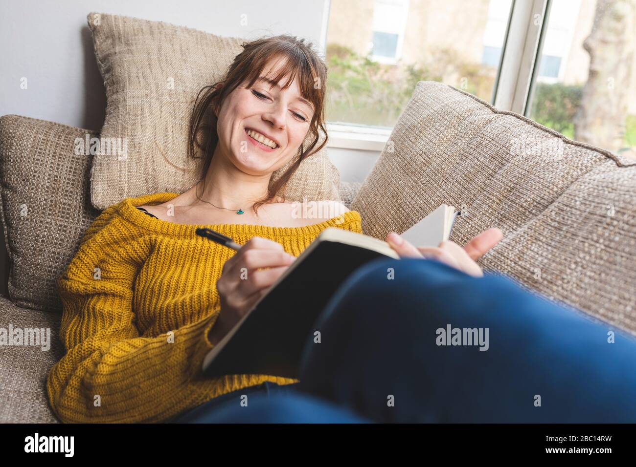 Portrait of happy woman lying on couch drawing in sketchbook Stock ...