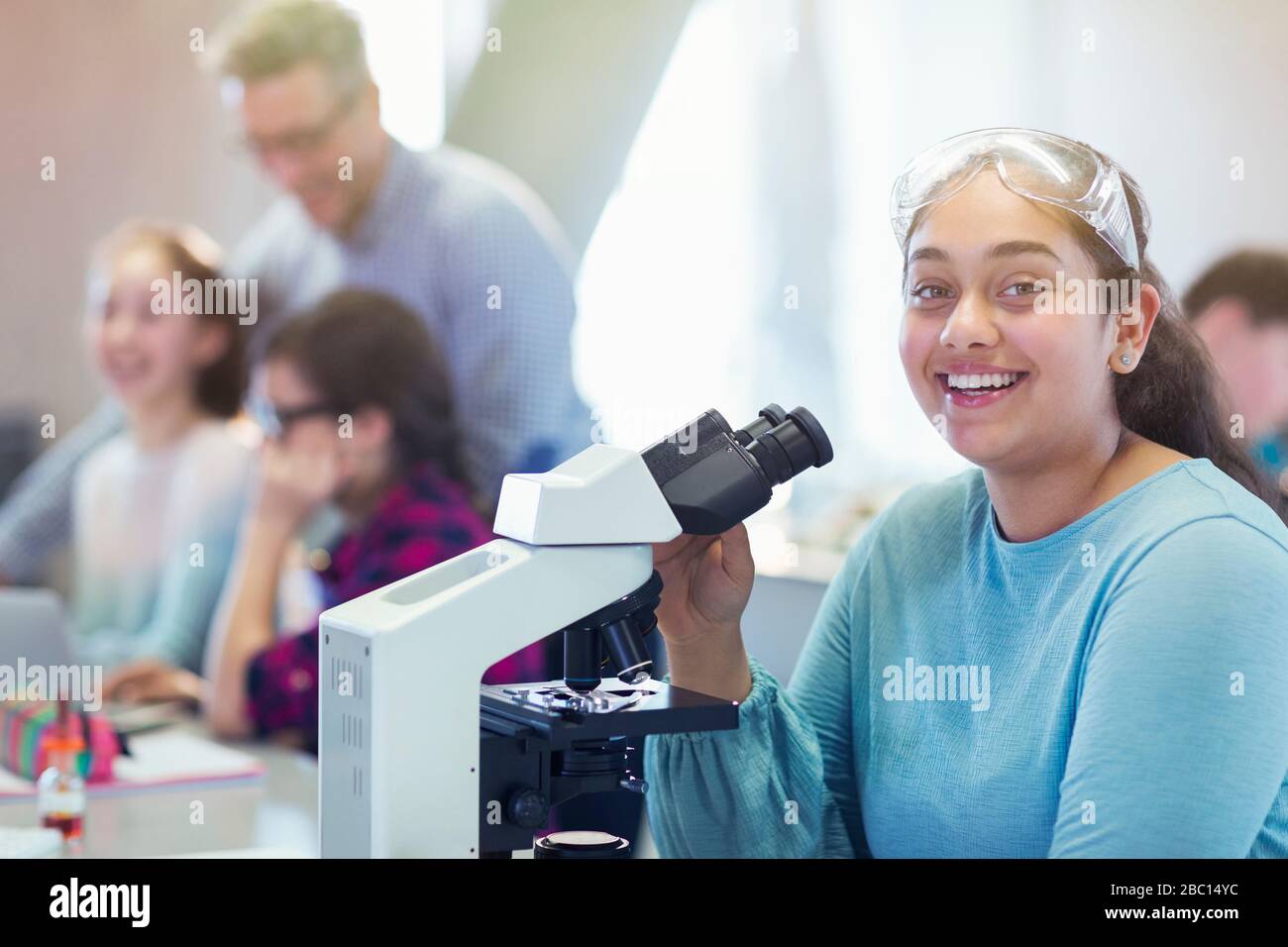 Portrait smiling, confident girl student conducting scientific experiment at microscope in laboratory classroom Stock Photo