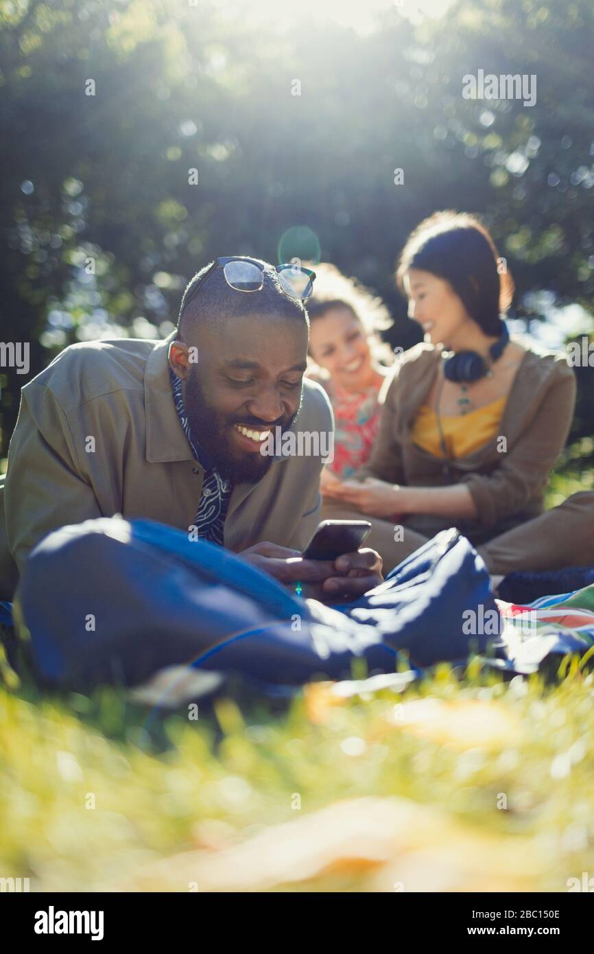 Smiling young man texting with cell phone and relaxing in sunny summer park Stock Photo