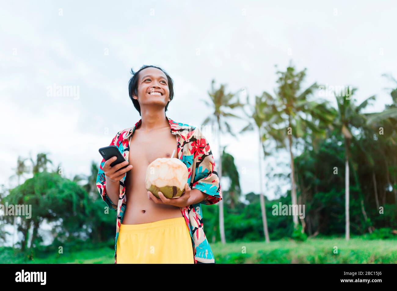 Portrait of happy man with smartphone and  fresh coconut, Borneo Island, Malaysia Stock Photo