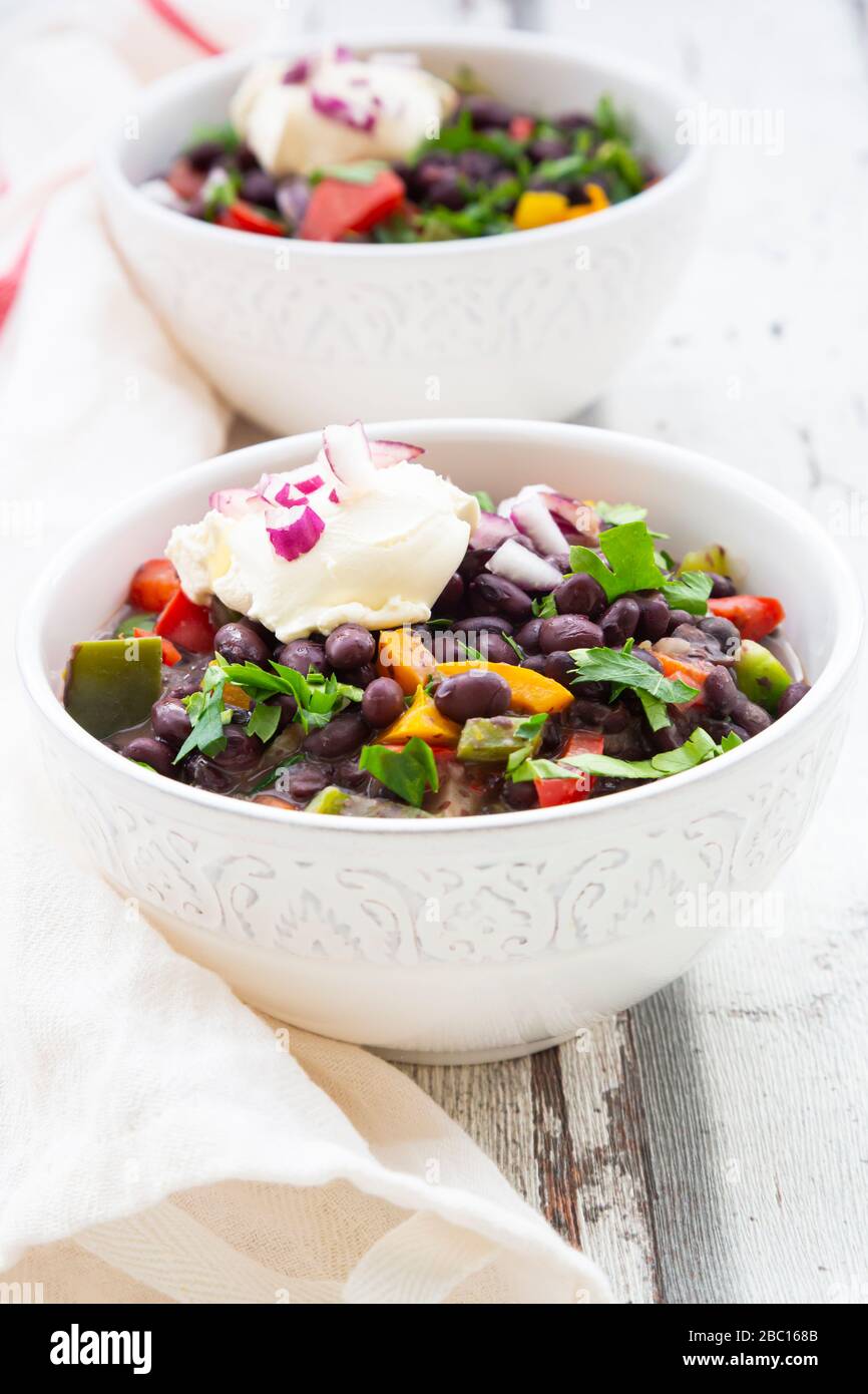 Two bowls of black bean soup with bell pepper, cilantro, sour cream and red onions Stock Photo