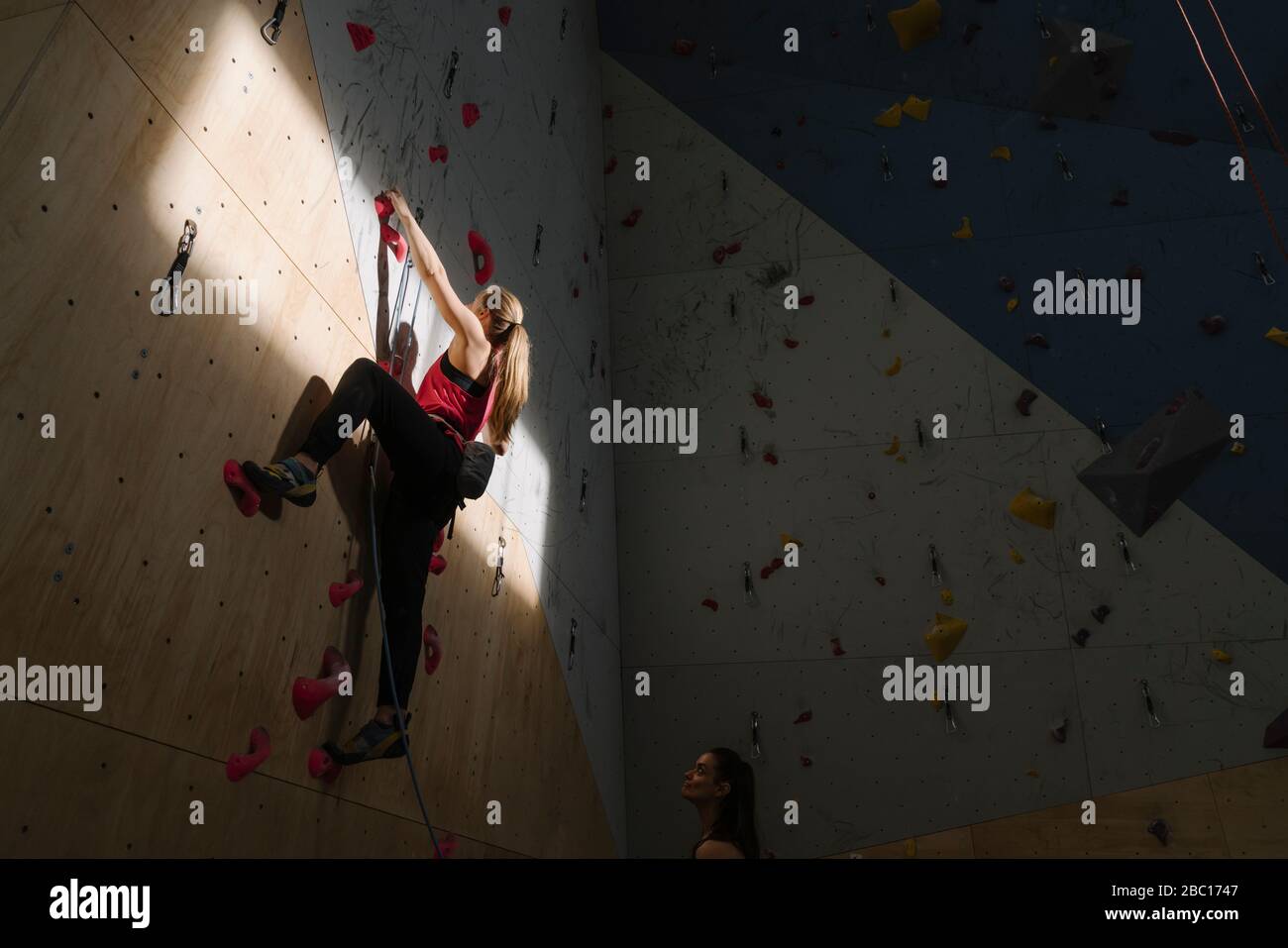 Woman climbing on the wall in climbing gym with sunlight and shadow Stock Photo