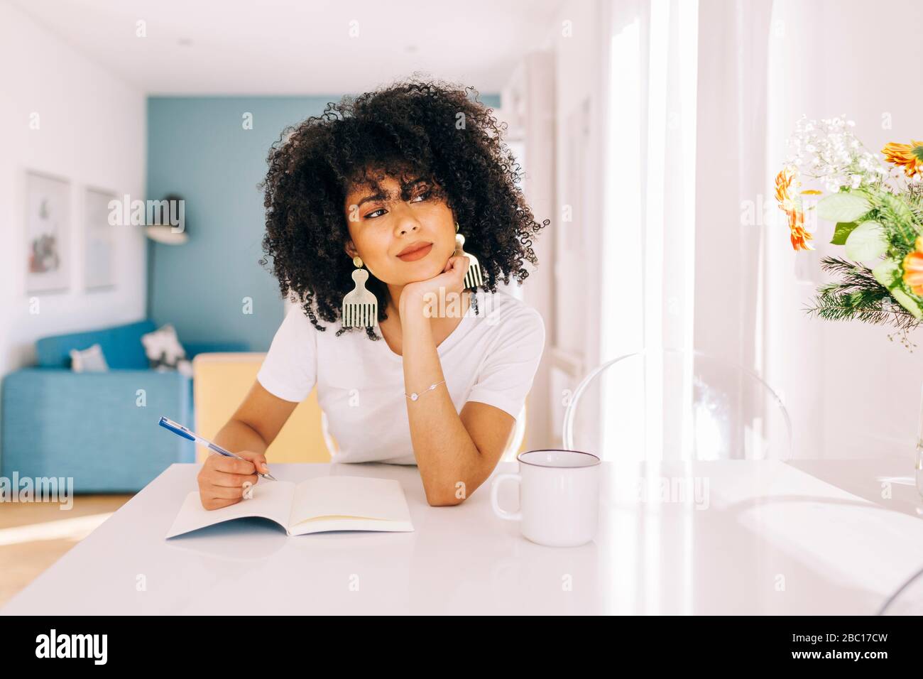 Portrait of young woman with curly hair sitting at a table with a notebook at home Stock Photo
