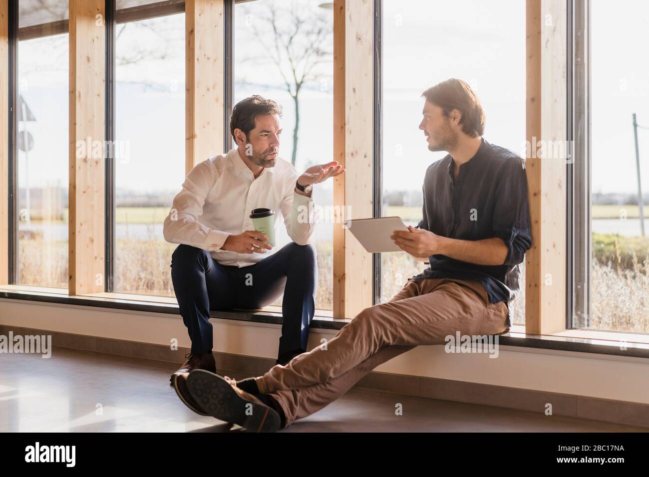 Two businessmen with tablet talking at the window in open-plan office ...