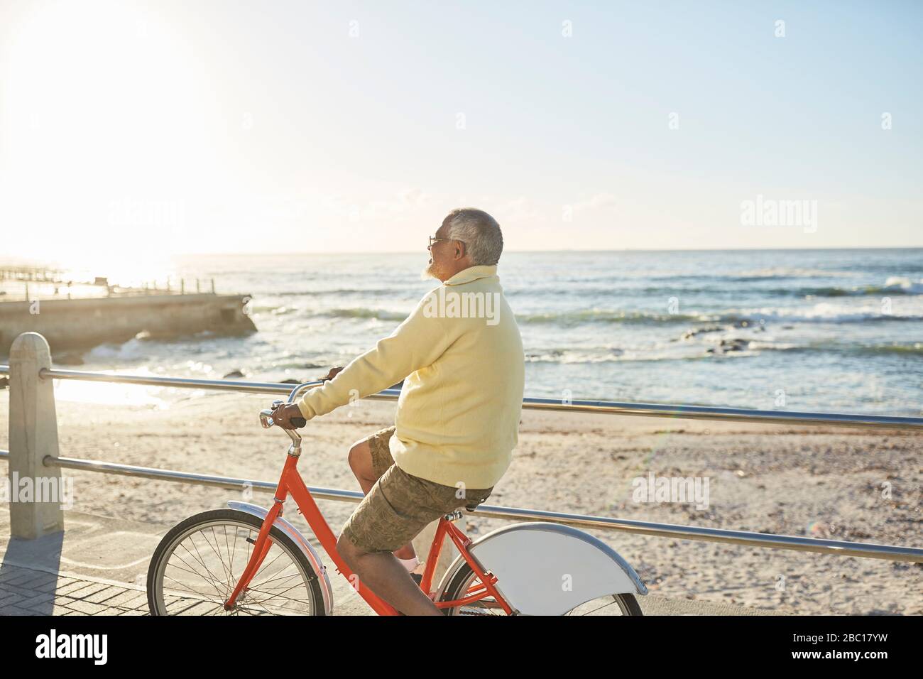 Active senior man tourist bike riding on sunny boardwalk along ocean Stock Photo