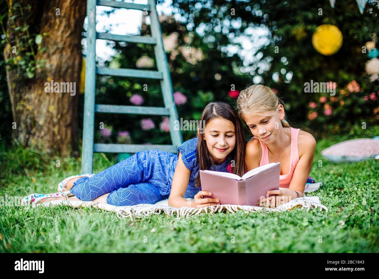 Smiling girls reading a book in garden together Stock Photo