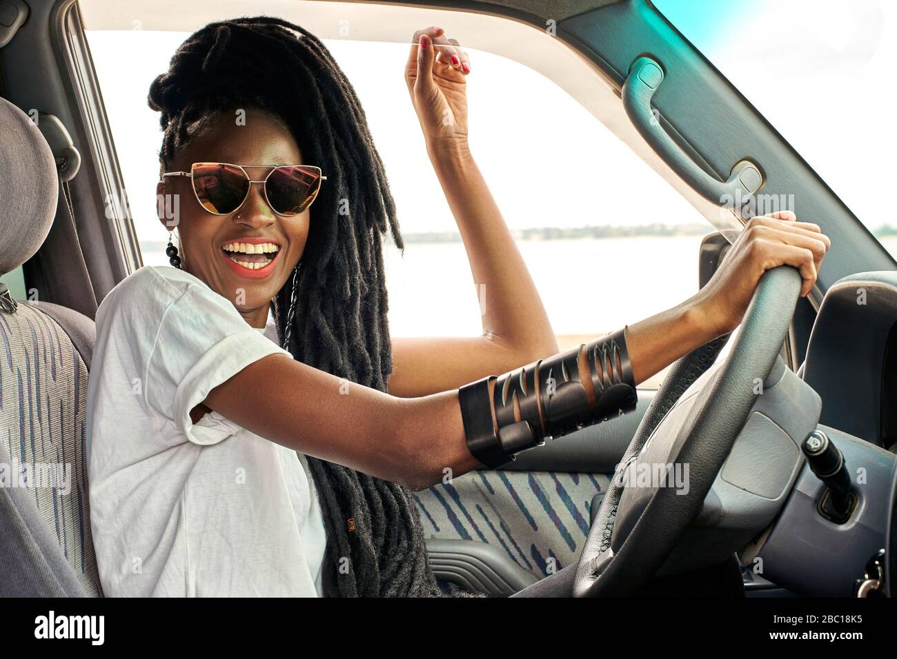 Portrait of laughing woman with dreadlocks driving car Stock Photo