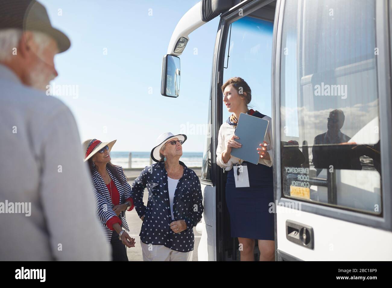 Tour guide talking to active senior tourists at doorway of tour bus Stock Photo