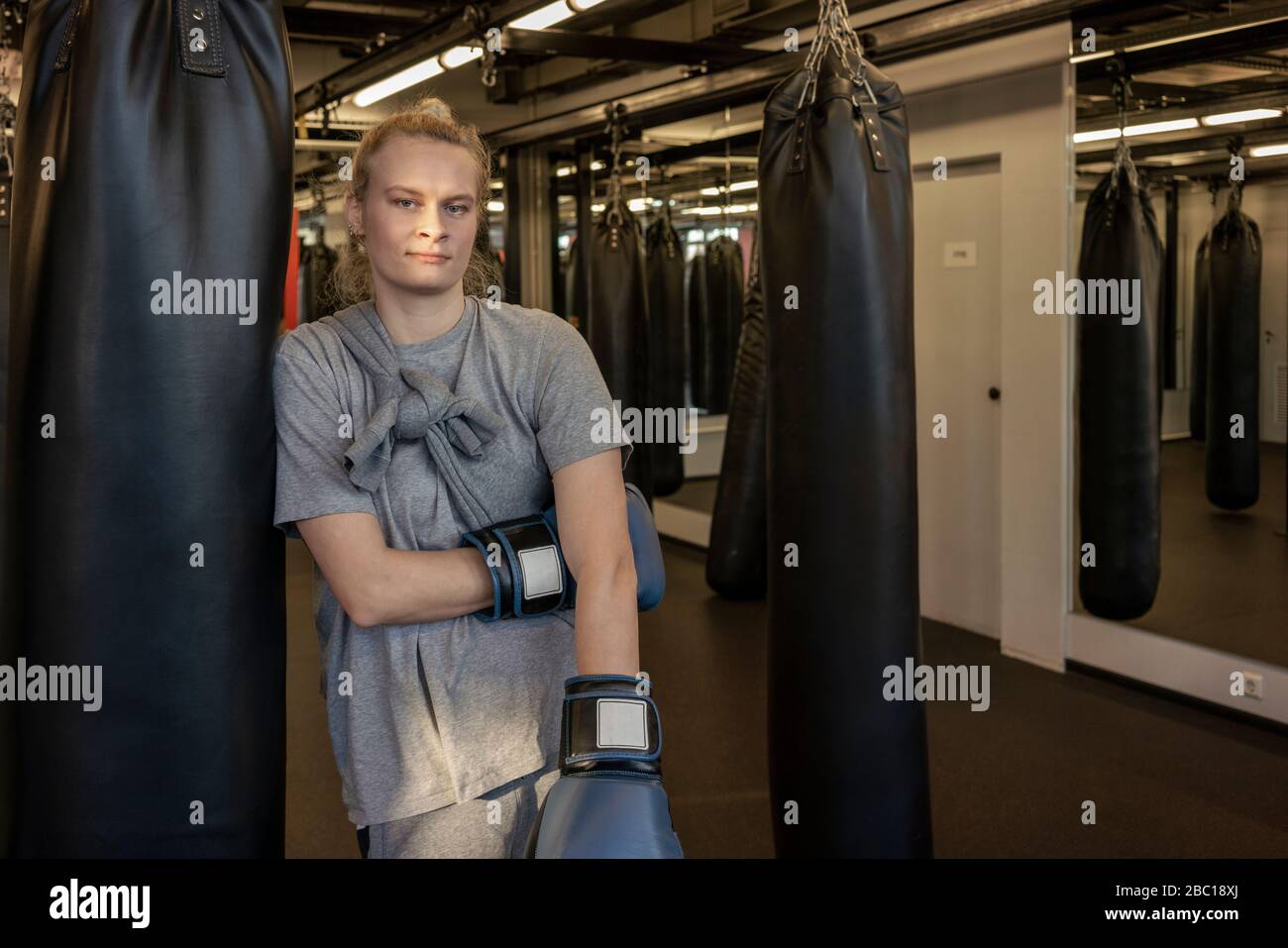 Portrait of woman with boxing gloves at sandbag in gym Stock Photo