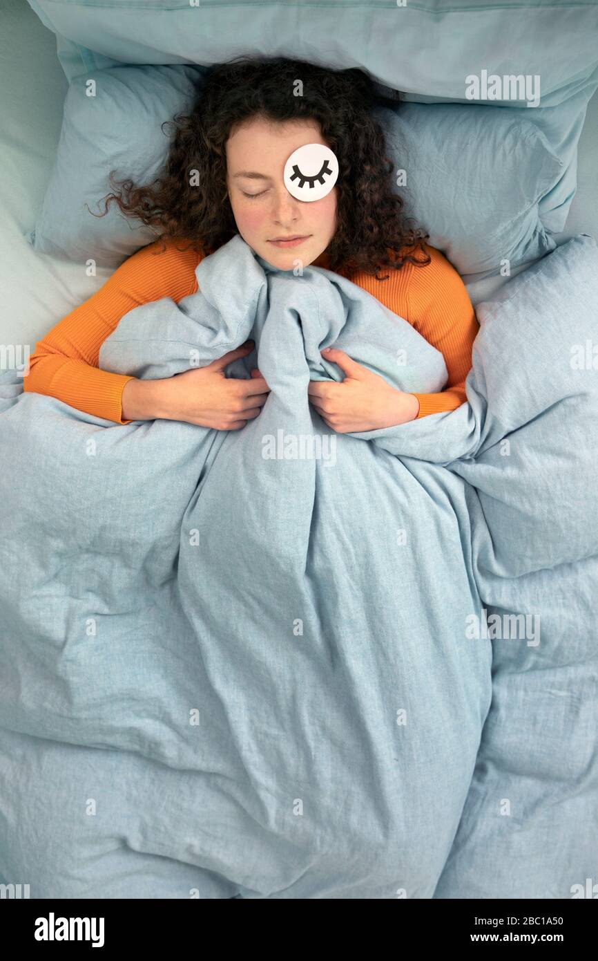 Portrait of sleeping young woman lying in bed with paper mask Stock Photo