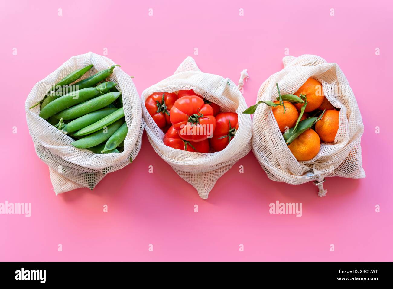 Eco-friendly reusable mesh bags with fresh green peas, tomatoes and clementines Stock Photo