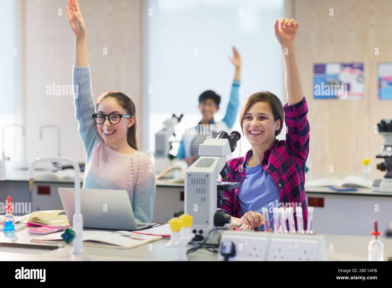 Eager, smiling students raising hands in science laboratory classroom Stock Photo