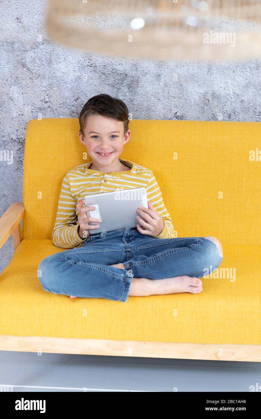 Boy playing with tablet on yellow couch Stock Photo