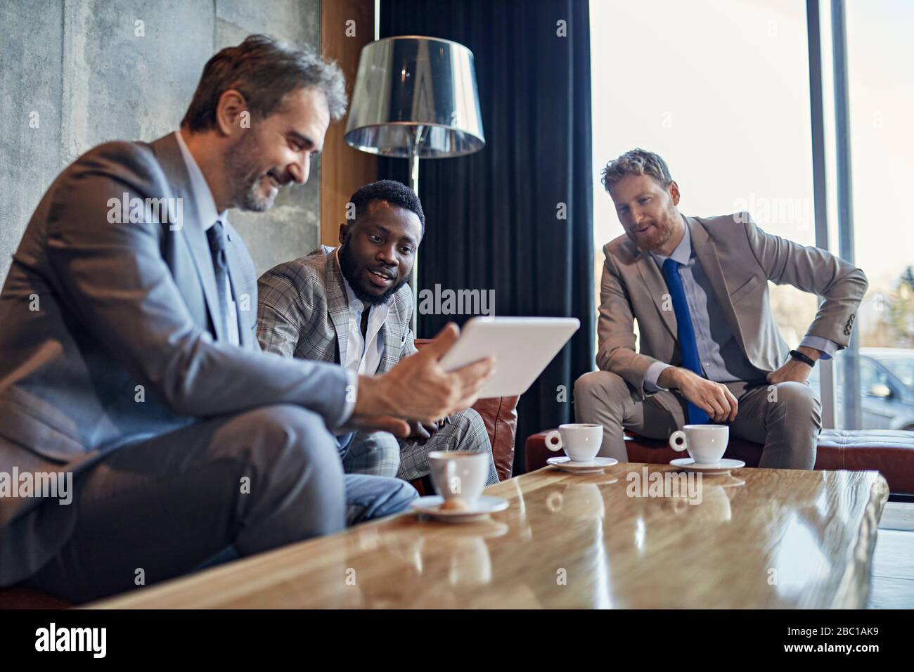 Three businessmen sitting in hotel lobby with tablet Stock Photo - Alamy