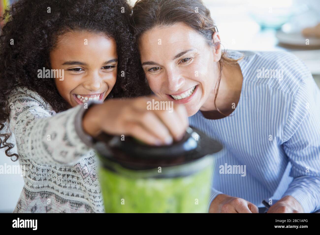 Mother and daughter making healthy green smoothie in blender Stock