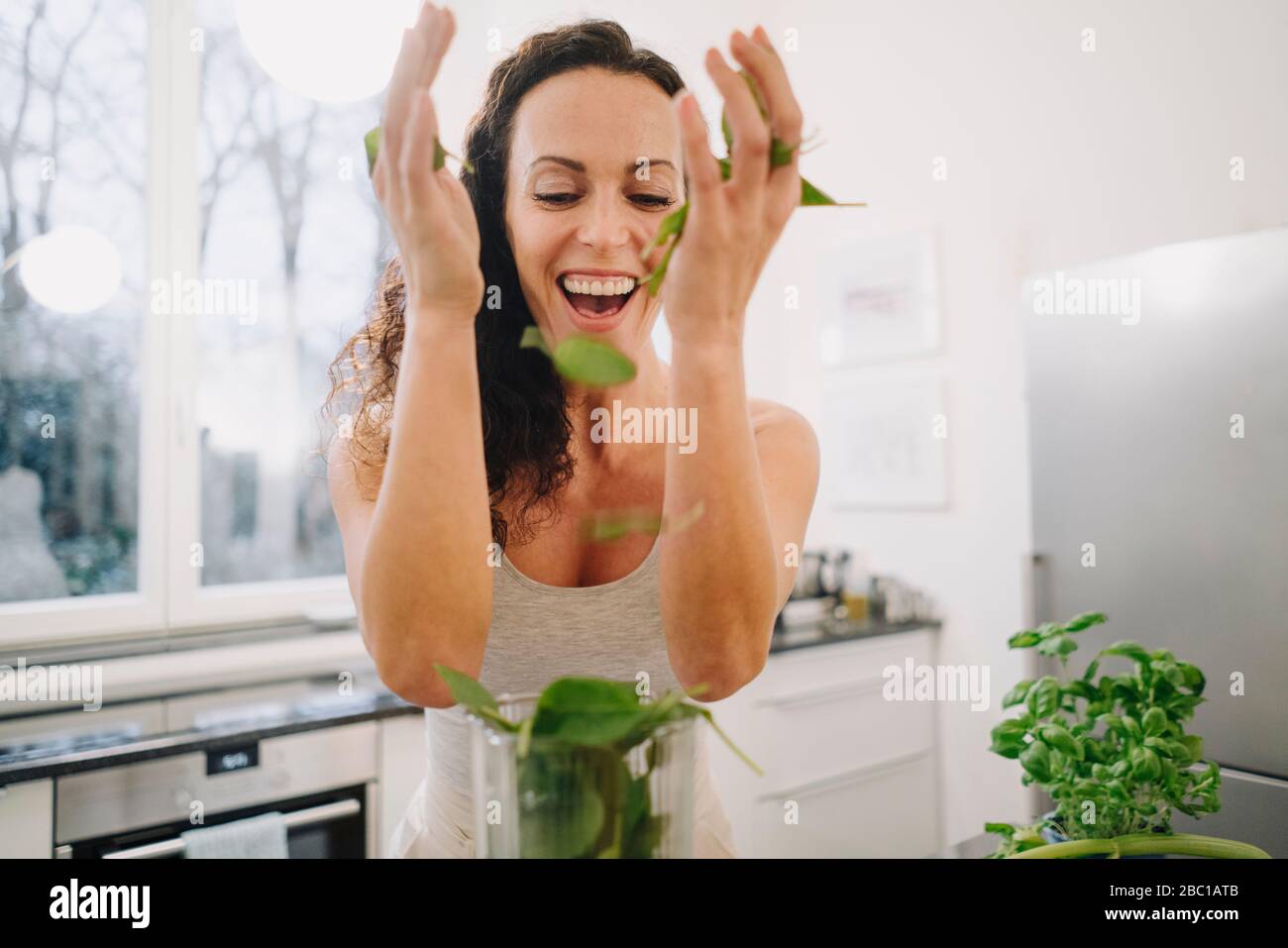 Fit woman standing in kitchen, preparing healthy smoothie, putting ingredients into blender Stock Photo