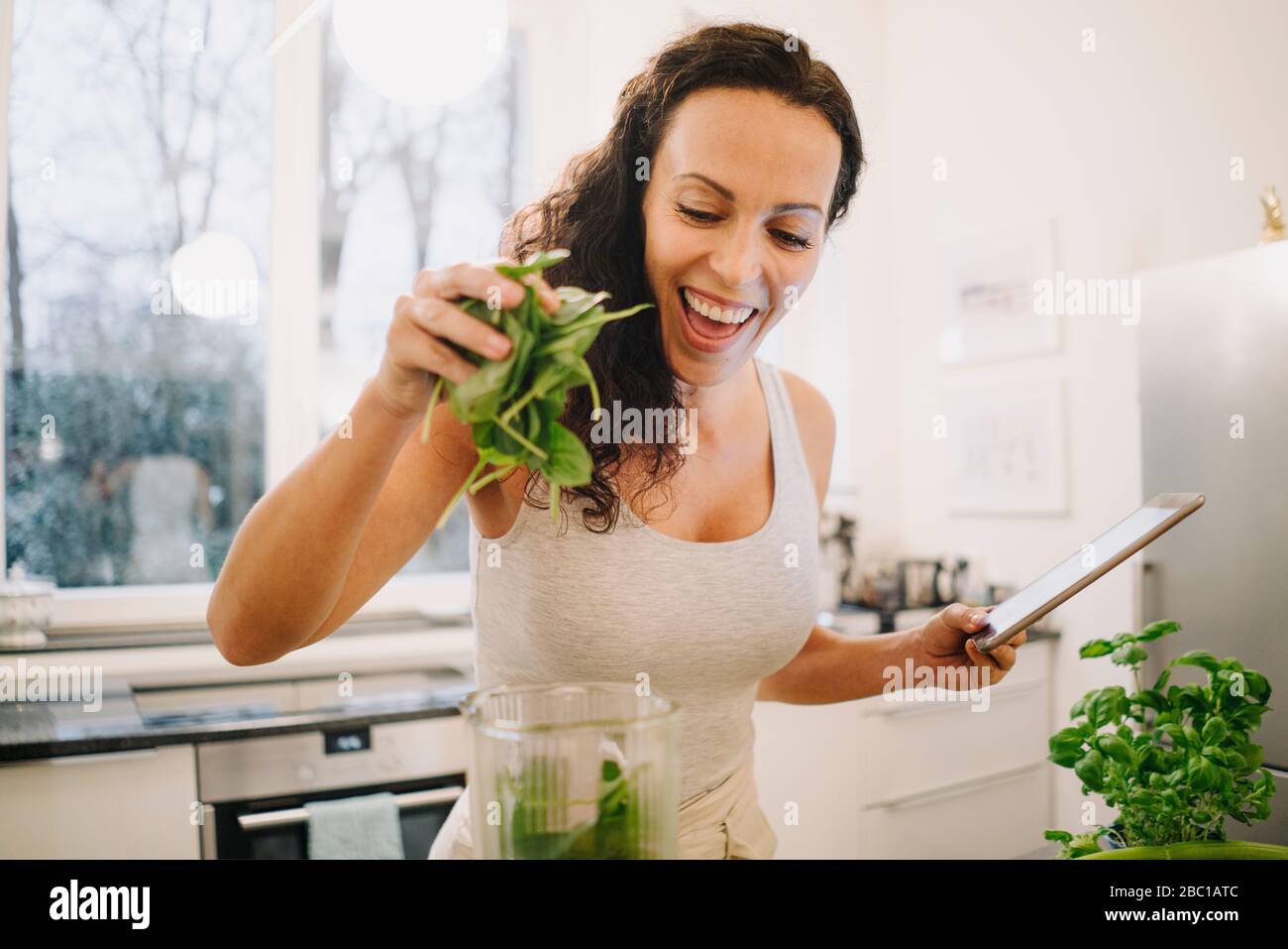 Fit woman standing in kitchen, preparing healthy smoothie, putting ingredients into blender Stock Photo