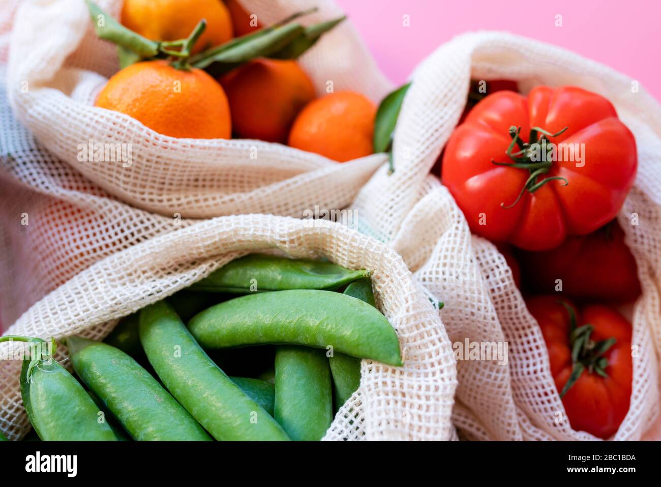 Eco-friendly reusable mesh bags with fresh green peas, tomatoes and clementines Stock Photo