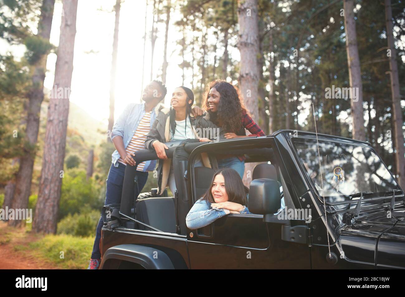 Young friends in jeep looking up at trees in woods, enjoying road trip Stock Photo