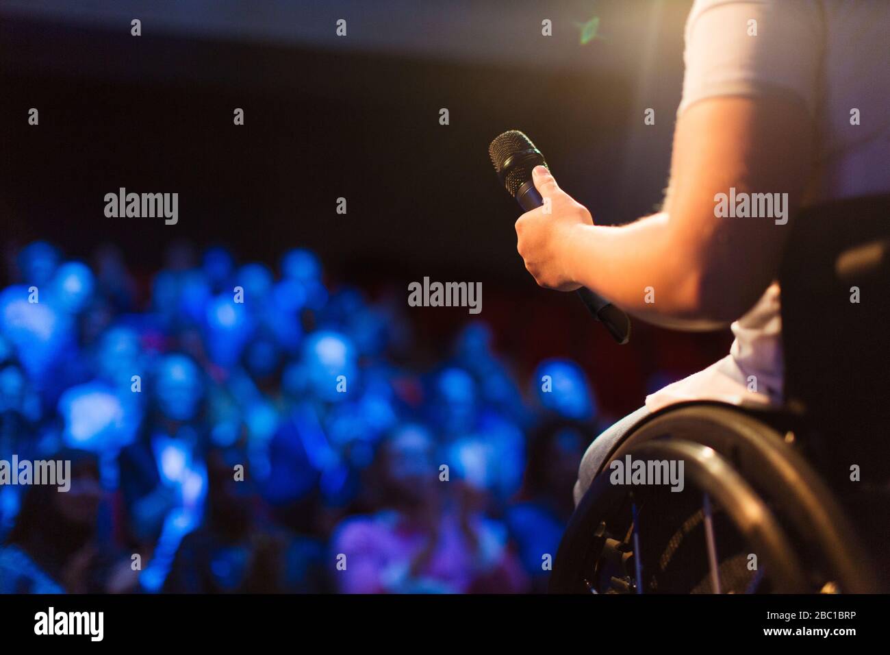 Female speaker in wheelchair holding microphone on stage Stock Photo