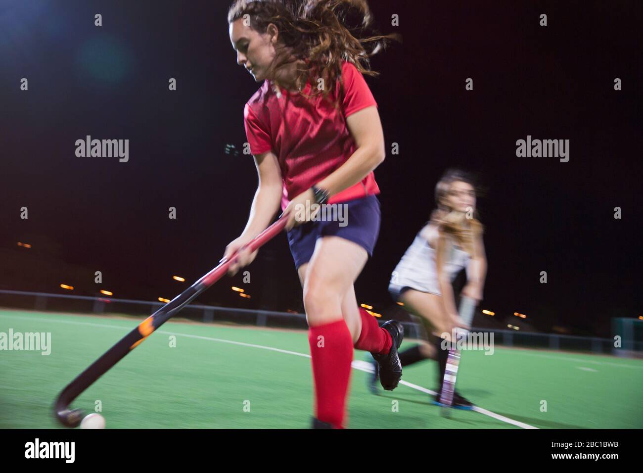 Determined young female field hockey player hitting the ball, playing