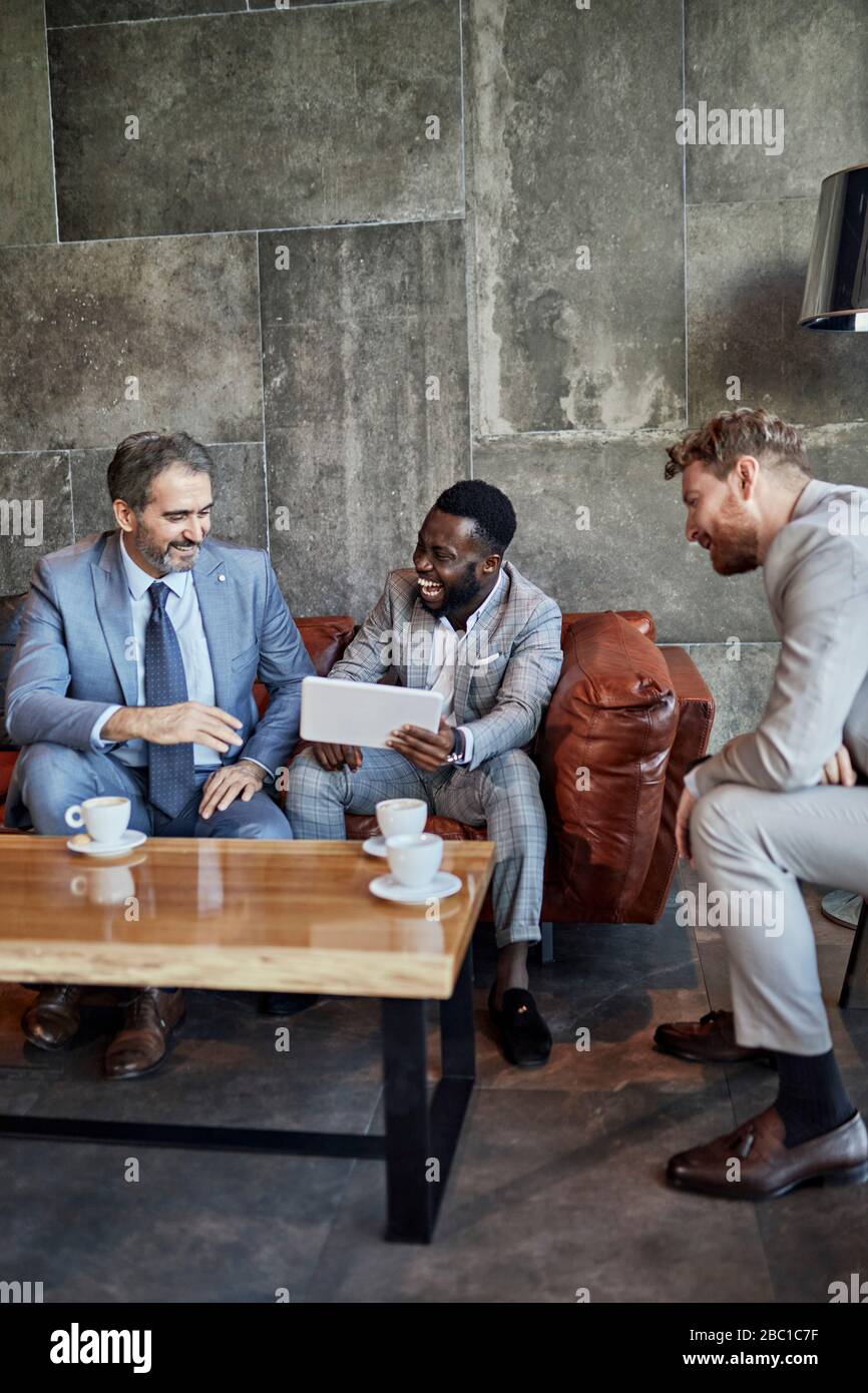 Three businessmen sitting in hotel lobby with tablet Stock Photo - Alamy