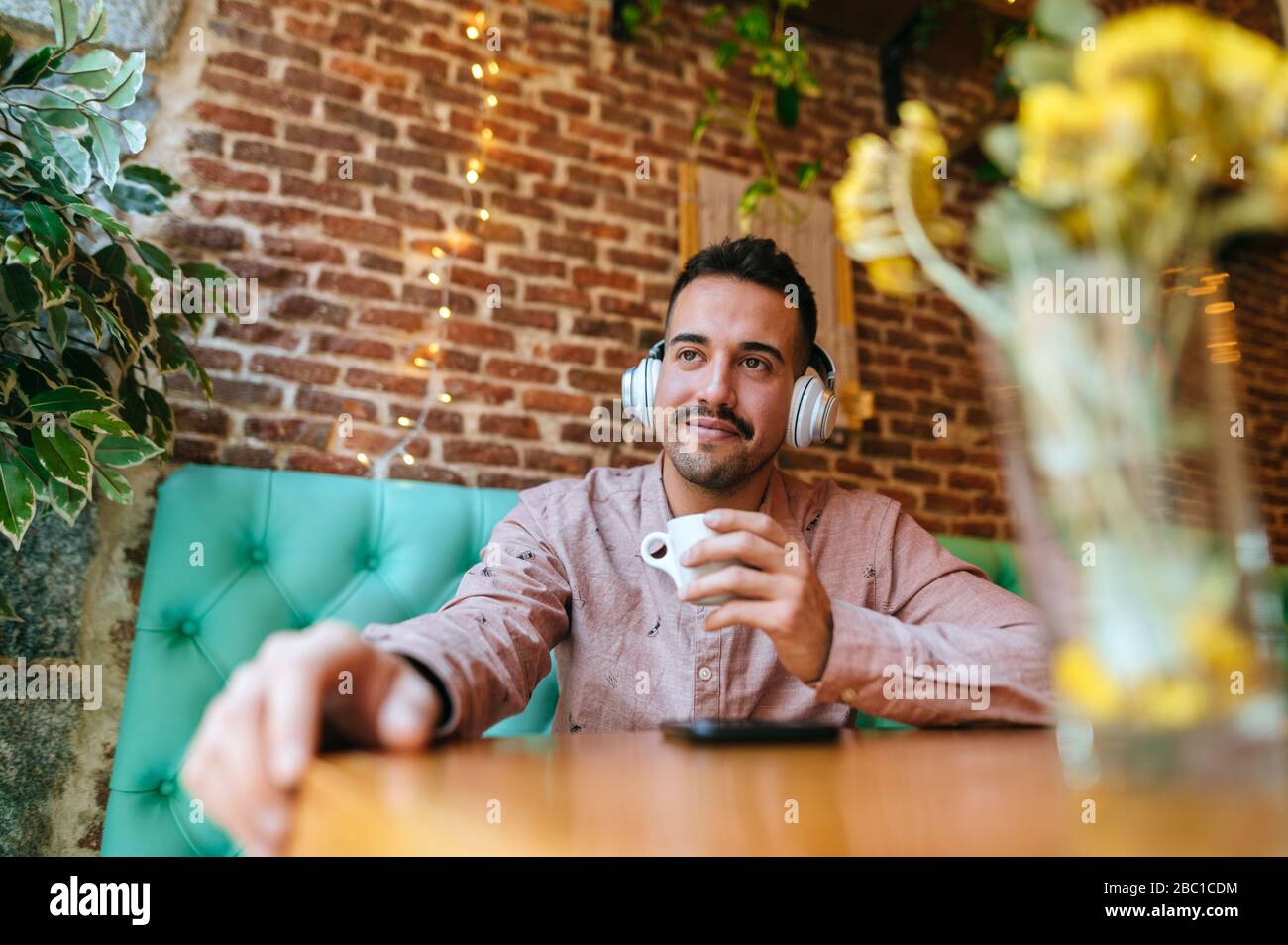 Smiling man in a cafe listening to music with headphones Stock Photo
