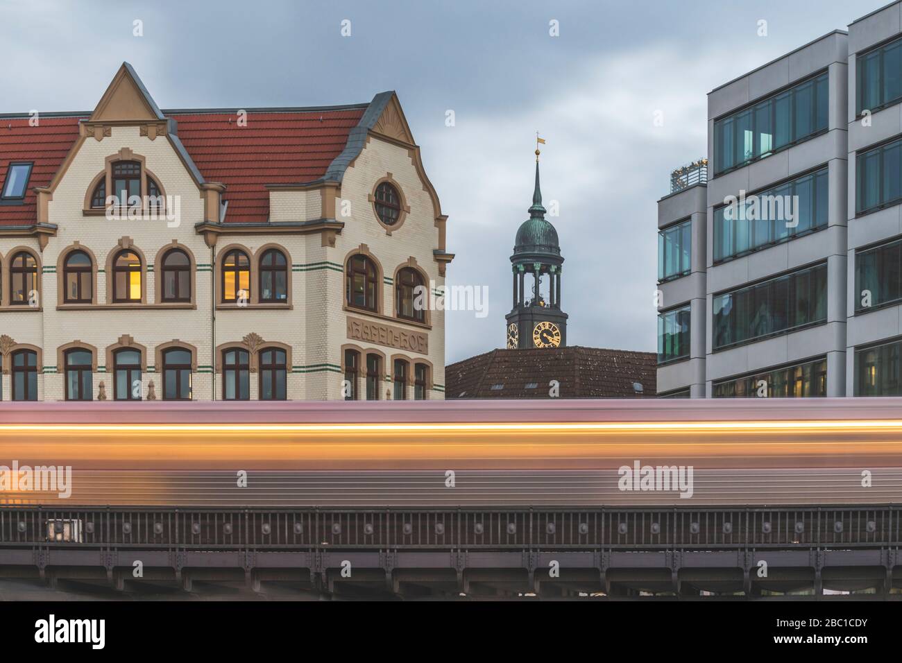 Germany, Hamburg, Blurred motion of elevated train passing residential building with tower of Saint Michaels Church in background Stock Photo