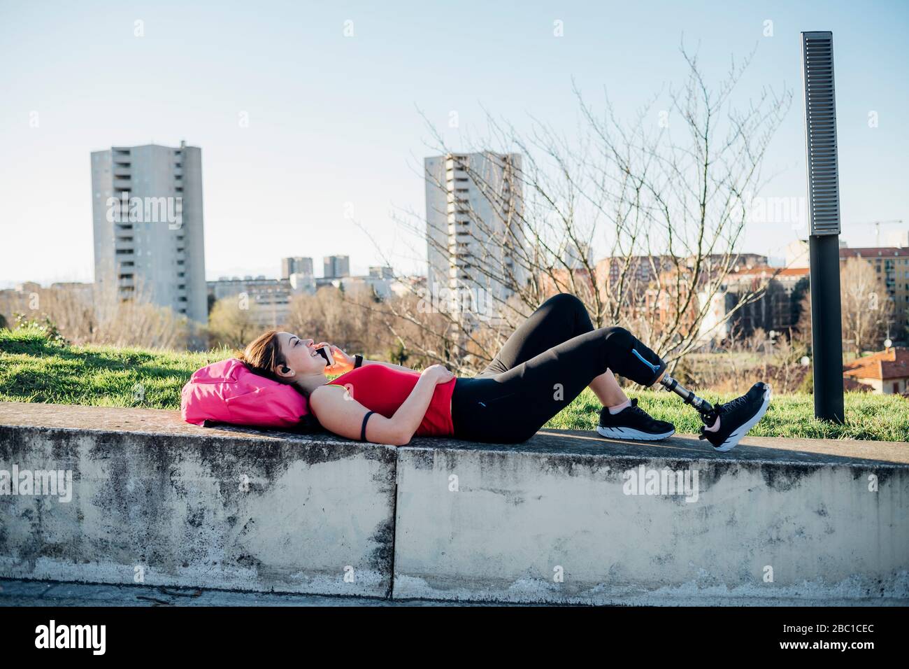 Sporty young woman with leg prosthesis lying on a wall talking on the phone Stock Photo