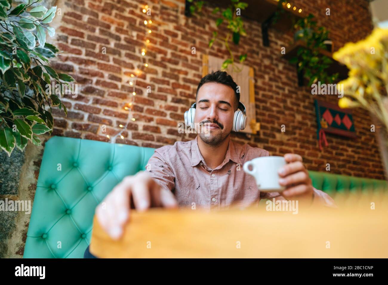Smiling man with eyes closed in a cafe listening to music with headphones Stock Photo