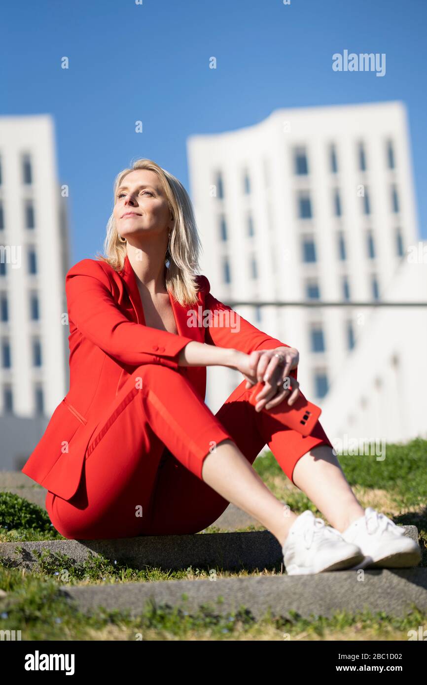 Blond businesswoman wearing red suit and sitting on stairs outdoor Stock Photo