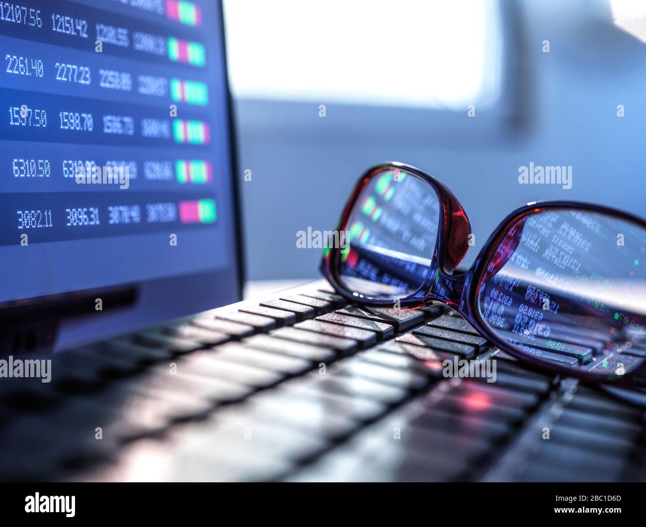 Stock market data reflecting in eyeglasses lying on laptop keyboard Stock Photo