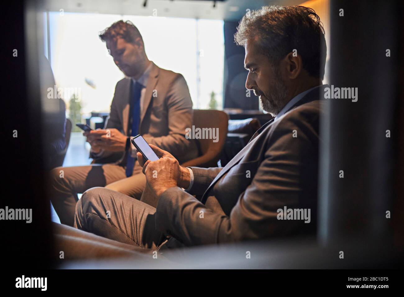 Two businessmen using smartphones in hotel lobby Stock Photo - Alamy