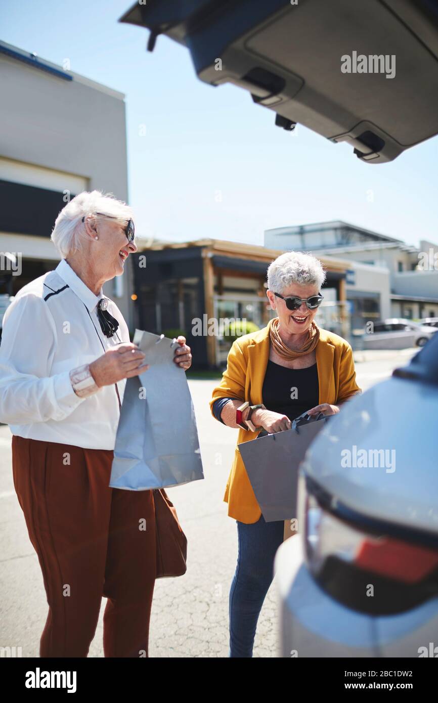Happy senior women friends loading shopping bags in back of SUV in mall parking lot Stock Photo