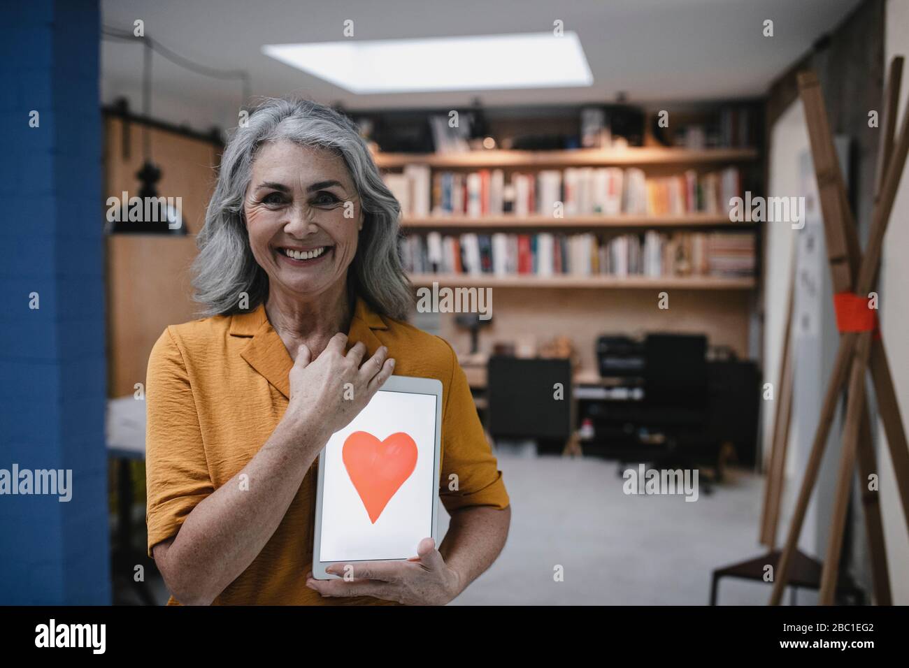 Smiling grey-haired woman holding tablet with a heart on the screen Stock Photo